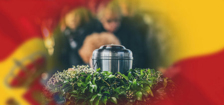 A metal urn with ashes of a dead person on a funeral, with people mourning in the background on a memorial service. Sad grieving moment at the end of a life. Last farewell to a person in an urn.の写真素材