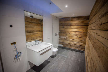 A modern bathroom with wooden walls and grey tiles on the floor. White tiles on the floor, bit mirror and a walk in shower with glass wall. Fancy looking home bathroom.の写真素材