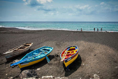 Three colorful wooden boats on a beach on the island of Santiago on Cabo Verde islands, with some people in the background.の写真素材