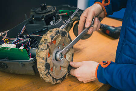 Serviceman stripping and removing wheels on robotic lawnmower, motorized lawnmower being serviced on a table after a year of use in the mud and grass. Regular maintenance of robotic lawnmowerの写真素材