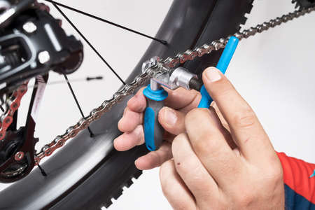 Bicicle repair or maintenance. Breaking the chain of a bicycle apart using a chain breaker tool in blue color. Splitting a bicycle chain with a tool.の写真素材