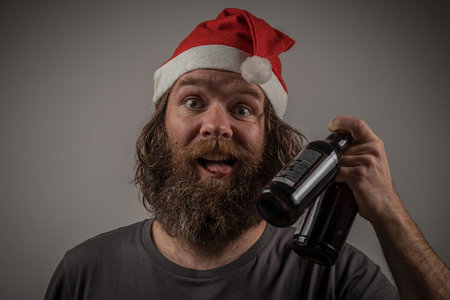 Bearded guy dressed as santa happy showing tongue and holding two craft beer bottles in hand. Expecting celebrations.の写真素材
