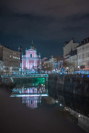 Ljubljanica river in Ljubljana Slovenia at night with visibile bridges and red francizskan church in the backgroundの写真素材
