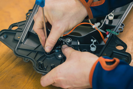 Serviceman stripping and removing components on robotic lawnmower, motorized lawnmower being...