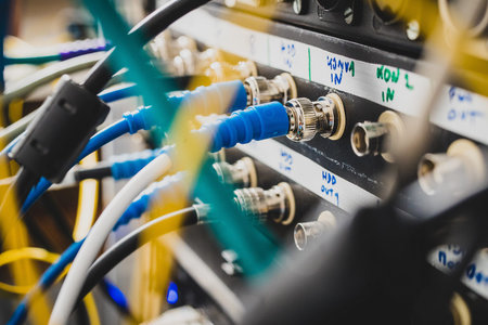 Blue BNC SDI signal cables plugged in the back of a patch panel. A mess of cables visible behind the...
