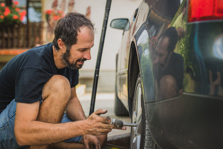Side view of a caucasian man unscrewing a modern  car wheel with a ratchet. Service of a car, changing tyres or wheels at home.の写真素材