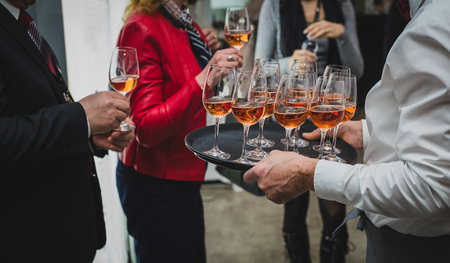 People taking glasses of rose wine from a tray held by a professional waiter or caterer. Catering with wine on a corporate event inside.の写真素材