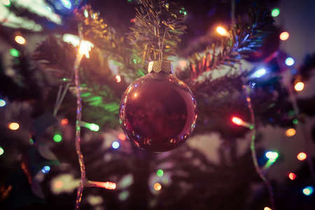 A ball ornament hanging on a christmas tree surrounded by lights on a tree out of focus.の写真素材
