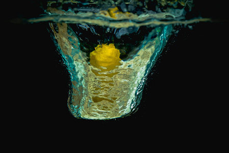 Fresh lemon half falls into water making big splash of drops and spray on a dark background. Juicy...