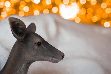 Head of a plastic deer posing in front of a white snow and some christmas decor lighting.の写真素材