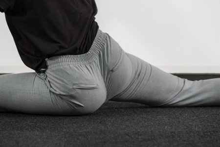 A young woman stretching and making a leg split in grey pants. Detail of tight buttocks and spread...