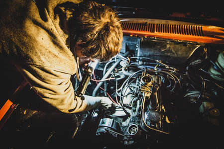 A man fixing an engine of a car at night. Vintage car being repaired during a night time. Bad timing for a car repair. Concept of a bad luck with a car.の写真素材