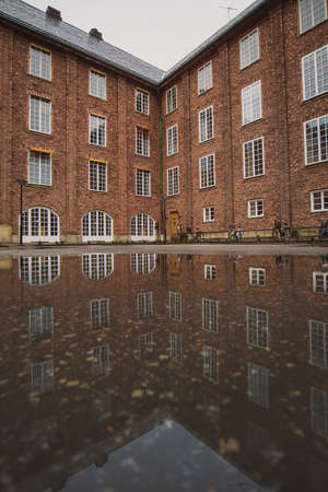 Large industrial red brick house, with visible reflection on the ground in a pool of water. Autumn cold setting, good for backgroundの写真素材