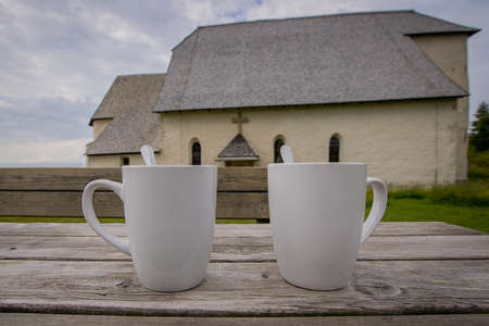 Two white coffe or tea mugs or cups on a wooden table. Church on the top of the hill in the background.の写真素材