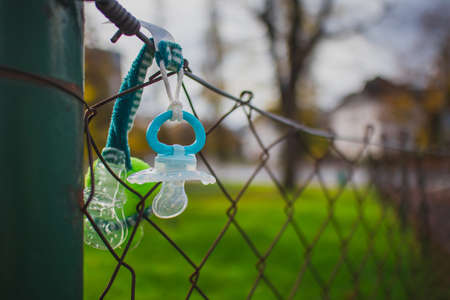 Lost child pacifier hanging on a metal fence waiting for the owner to come back. Dirty plastic kid pacifier lost outdoors.の写真素材