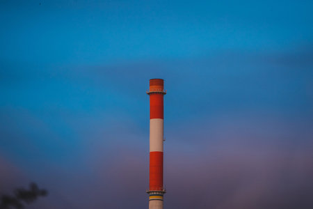 A tall single red and white chimney or smoke stack on a blurred cloudy background. No smoke from the...