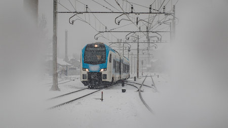 Modern commuter passenger train is rushing through the dense snowfall or snow which is hindering...