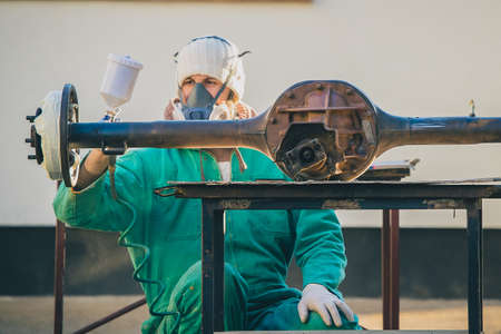 Man with automotive air spray gun in action during the restoration of a vintage car. Applying first base layer of paint onto an old big differential unit or rear axle.の写真素材