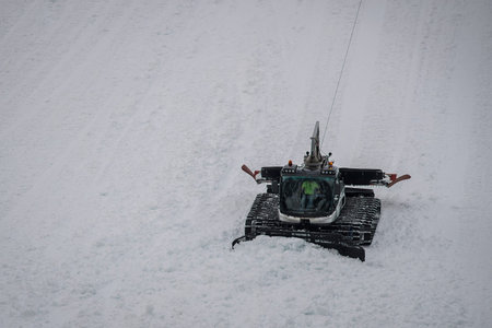 Snow groomer working on a very steep terrain, using a winch and a rope as a security guard. Groomer...