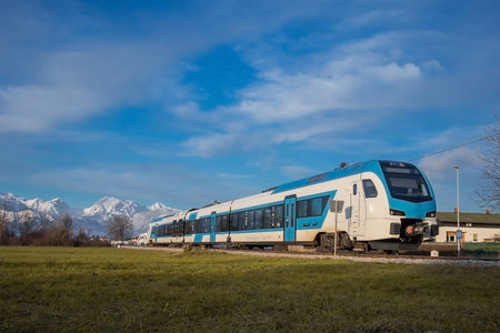 Modern diesel passenger train in white and blue color approaching small station of Rodica on a sunny...