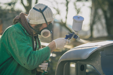 Man with automotive air spray gun in action during the restoration of a vintage car. Applying first base layer of paint onto bare metal.の写真素材