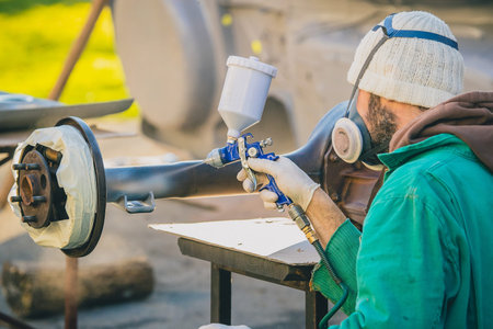 Man with automotive air spray gun in action during the restoration of a vintage car. Applying first...