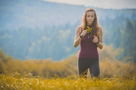 Cute beautiful caucasian girl walking through golden meadow while holding different herbs in her hand. Autumn setting on a grassy meadowの写真素材