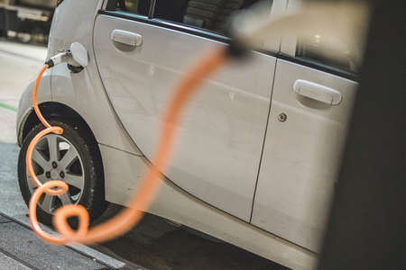 Small city electric car plugged in charging station. Orange charging cable is visible connected to inlet port of an electric car.の写真素材