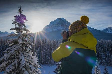 A Man is photographing beautiful snowy mountain scenery. Man in winter clothes and telephoto lens taking pictures of a beautiful mountain landscape. Picture from side and back.の写真素材