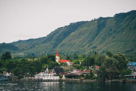 Volcanic Island of Samosir on the lake of Toba, on northern Sumatra, Visible typical houses and christian church on the island on a cloudy day.の写真素材