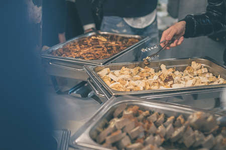 Hands of people seen taking food out of stainless steel containers at a buffet or catering gala event. Tasty food being served on a catering event.の写真素材