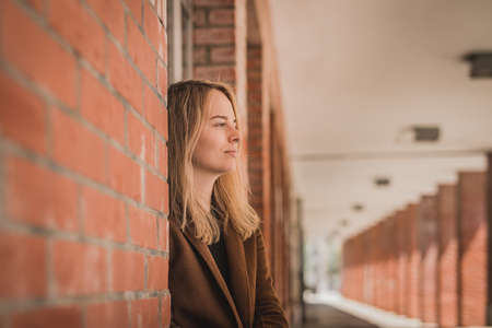 Cute fashionable young woman in a red brick hallway looking away in the distance. Caucasian girl in a let's go mode, wanting to travel. Wanderlust hipster girl smiling. Copy space on the left.の写真素材