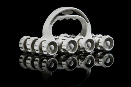 White plastic massager with wheels isolated on black with reflection on the bottom. Side view of plastic vintage roller massager.の写真素材