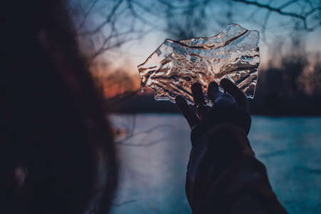 Silhouette of a hand holding a piece of ice block from a pond. Cold and winter feeling, looking through icy patch.の写真素材