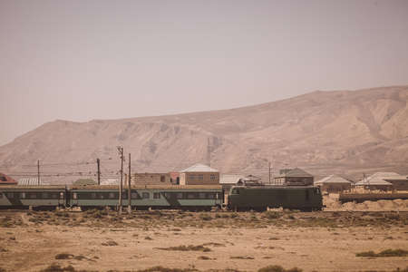 Side view of electric passenger train with green locomotive and passenger coaches in the plains or deserts of Azerbaijan, close to Baku.の写真素材