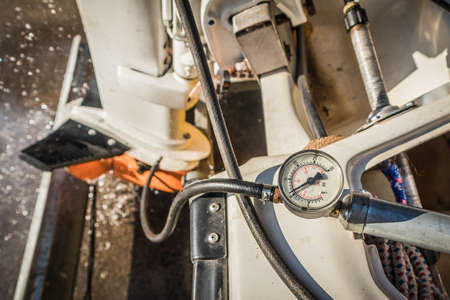 Servicing the lower unit of an outboard engine - the gearbox. Testing the sealing of the gearbox of an engine, with pressure gauge visible and working engine in the background.の写真素材