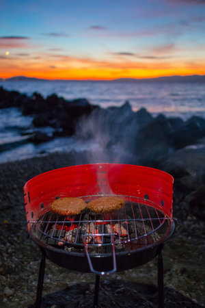 Grilling burgers on a small metal portable charcoal grill on the shores of Lac Leman in Switzerland...