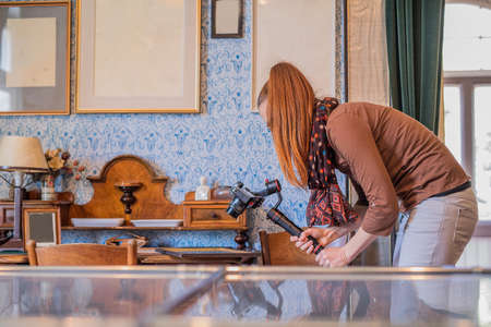 Young woman using a gimbal camera stabilizer to take footage inside a house. Filming different antiques using a professional modern mirrorles camera.の写真素材