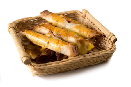 Batch of freshly baked taquitos in a wicker basket serving, on a white isolated background. Tasty mexican snack fresh out of the oven. Side viewの写真素材