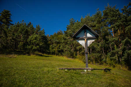wooden crucifix with jesus on the meadow on top of the hill, surrounded by a forest on a sunny summer day.の写真素材