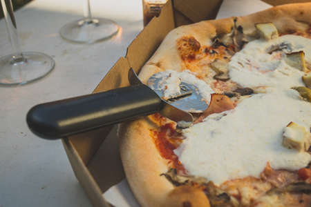 Round pizza slicer resting on a pizza. Dirty slicer with black handle and round shiny blade.の写真素材