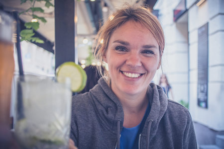 A young caucasian woman enjoying a glass of gin tonic with a lime and cheering with another person...