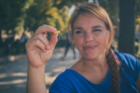 A young caucasian woman holding a nut and looking at it while enjoying sun in a park in Budapest, Hungary while wearing a blue shirt.の写真素材