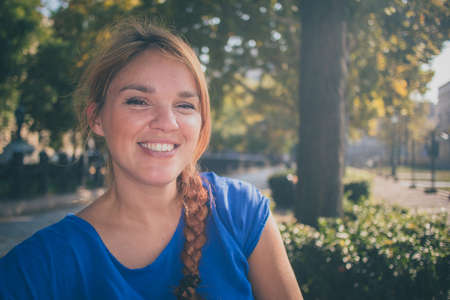 A young caucasian woman smiling and enjoying the autumn sun in a park in Budapest, Hungary while wearing a blue shirt.の写真素材