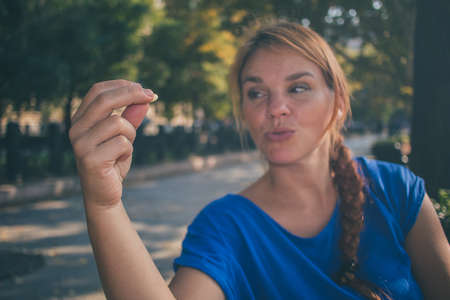 A young caucasian woman holding a nut and looking at it while enjoying sun in a park in Budapest, Hungary while wearing a blue shirt.の写真素材