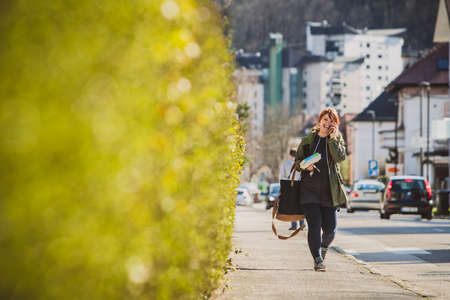 Woman walking towards the camera smiling, talking on the telephone and carrying full load of bags, eggs and car keys. Woman in suburban environmet in europe carrying too much stuff.の写真素材