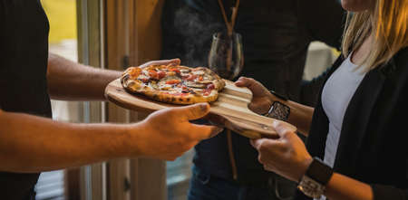 Man and a woman exchanging a fresh home made italian style pizza as a gift at a celebration. Steaming hot pizza as a giftの写真素材