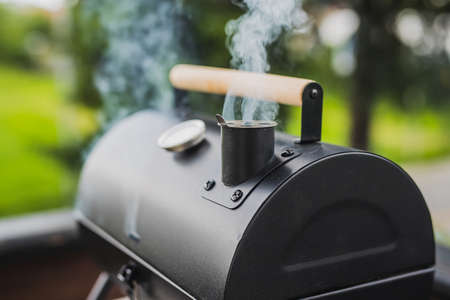 Smoke coming out of a smokestack of a small black smoker grill or barbecue on green background.の写真素材