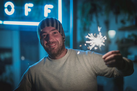 Young man in a hat with a sparkler or spark stick in his hand in a happy mood outside. Celebrating in the cold outside, wearning just a sweater.の写真素材