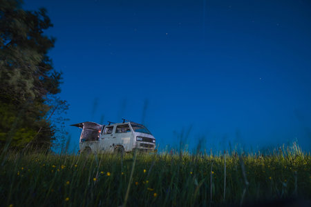 vintage adventure campervan is parked on a green meadow with flowers during a bright starry night....
